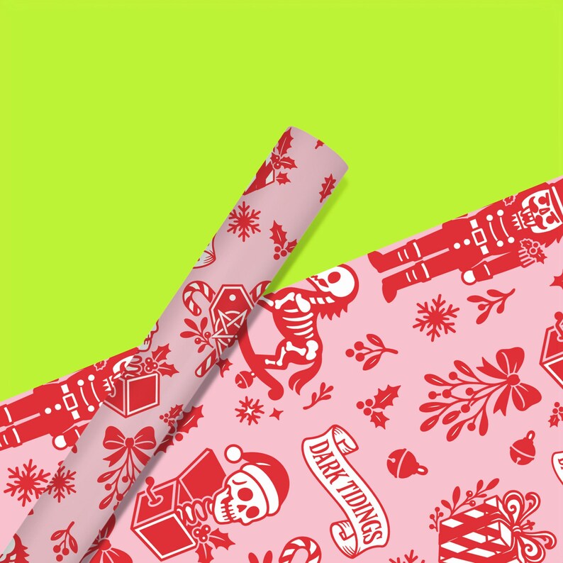 Premium satin finish wrapping paper featuring a repeating pastel goth pattern on a pink background. The design showcases a playful yet spooky aesthetic with high-contrast skeleton nutcrackers, skull jack-in-the-boxes, and rocking horse skeletons in soft pinks, and reds. The paper texture appears semi-glossy. Shown in three available sizes including sheets and rolls, specifically 29 inches wide, suitable for wrapping gifts for holidays, birthdays, or gothic themed occasions.