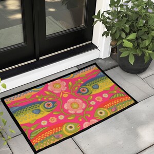 Rectangular indoor outdoor doormat featuring a vibrant hot pink background with a symmetrical maximalist pattern. The design showcases stylized sardines in yellow, lime green, and cobalt blue swimming horizontally towards a central vertical axis of blooming pale pink flowers and green vines. The imagery mimics the texture of vintage needlepoint embroidery but is a flat print on polyester. The mat is framed by a sleek black trim and features a non-slip rubber backing for safety.