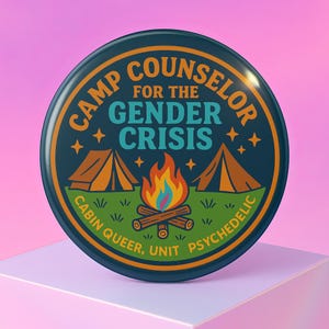 May include: A circular badge with a navy blue background, featuring the text "CAMP COUNSELOR FOR THE GENDER CRISIS." The design includes orange tents, a campfire, and the words "CABIN QUEER, UNIT PSYCHEDELIC."