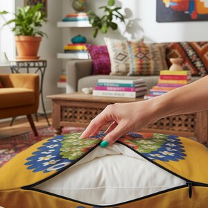 A square throw pillow featuring a vibrant Virgo zodiac design on a golden mustard yellow background. The central illustration shows a terracotta-skinned figure with green hair adorned with white daisies. Blue leaf motifs are printed on the figure’s chest. The word "VIRGO" appears in white bubble letters at the top. The entire design is framed by a royal blue scalloped border, featuring a high-fidelity trompe-l'œil print that mimics 3D embroidery.