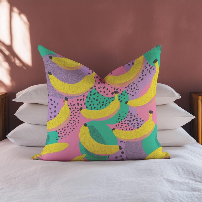 Square pillowcase featuring a bold and playful banana print in a vibrant pop art style. The design includes bright yellow bananas layered over a backdrop of pink, purple, green, and teal with dotted and speckled textures for a dynamic, retro-inspired look. Made of smooth fabric with crisp edges and a snug fit, the pillowcase showcases a saturated, high-contrast palette perfect for maximalist or dopamine decor. Pillow cover only; insert not included.