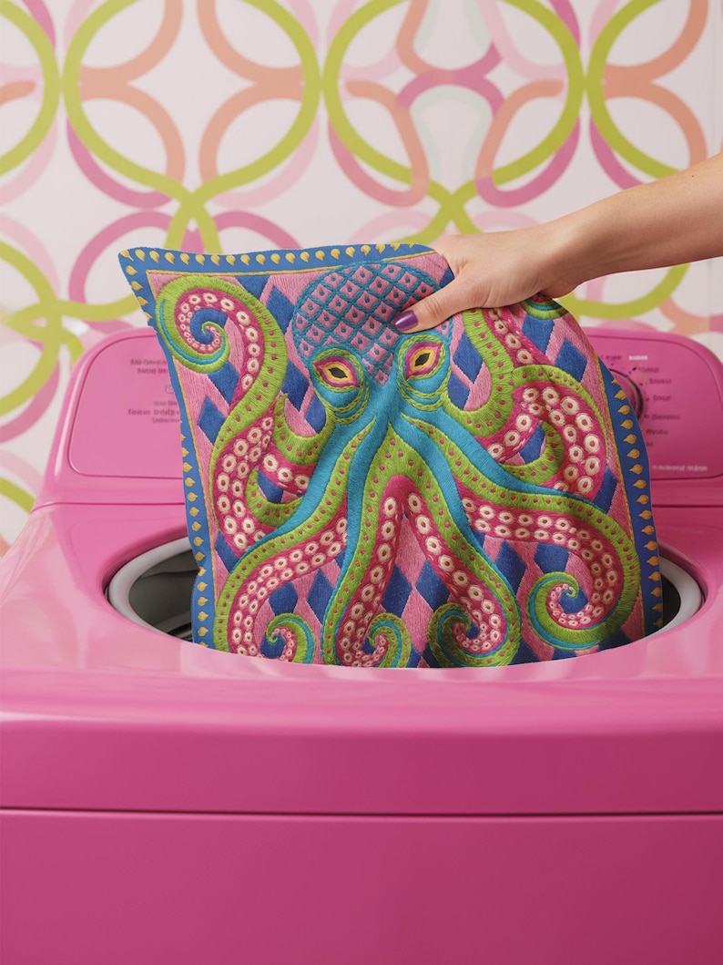 A square decorative throw pillow cover featuring a highly symmetrical bright octopus design. The octopus has a turquoise blue body with a diamond patterned head and eight curled tentacles detailed in bright pink and lime green. The background is a repeating diamond argyle pattern in royal blue and light pink. The artwork is a flat two dimensional print that mimics the textured look of intricate crewelwork embroidery. The pillow features a hidden zipper on the bottom edge. No insert included.