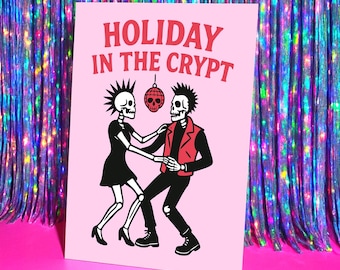 May include: A pink card with the text "HOLIDAY IN THE CRYPT" in red. The card features a black and white illustration of two skeletons dancing. One skeleton wears a black dress, and the other wears a red jacket.
