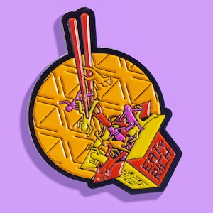 Può includere: Un cono di cialda giallo e arancione pieno di figurine di bastoncino rosa e giallo. Il cono è sormontato da due bacchette rosse. Il testo "Eat the Rich" è stampato sul lato del cono.