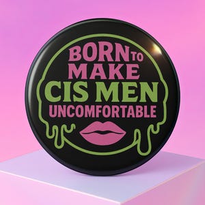 Puede incluir: Un botón redondo negro con el texto "BORN TO MAKE CIS MEN UNCOMFORTABLE" en rosa y verde. El diseño incluye un gráfico de labios rosas y un contorno verde. El botón está sobre una superficie blanca sobre un fondo rosa.