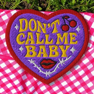 Peut inclure: Écusson brodé en forme de cœur avec le texte "DON'T CALL ME BABY" en jaune. Le patch a un centre violet, une bordure rouge et représente des cerises, des lèvres et des étoiles. Le patch est sur un fond à carreaux roses et blancs.