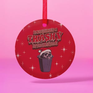 以下が含まれることがあります： 白い星の模様がついた赤い丸いクリスマスオーナメント。オーナメントには、ゴミ箱の中にサンタの帽子をかぶった白黒の漫画のアナグマが描かれています。オーナメントの文字は「Have Yourself a Trashy Little Christmas」です。