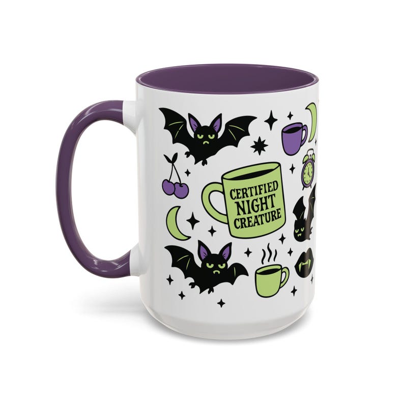 White ceramic mug with vibrant purple interior and matching C-handle. Features a full wrap-around, 'spooky cute' pastel goth design. Central graphic is a lime green coffee cup with 'CERTIFIED NIGHT CREATURE' in black text. Surrounding illustrations include grumpy black bats, a steaming green coffee cup, a purple mug, vampire fangs, crescent moon, black cherries, and an alarm clock. Design uses bold graphics in black, lime green, and purple, accented with small black stars. Pastel Goth vibes.