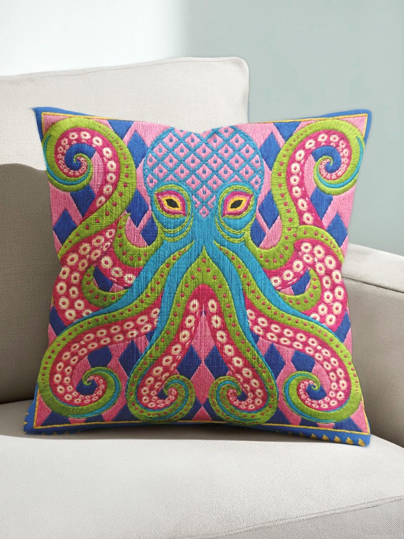 A square decorative throw pillow cover featuring a highly symmetrical bright octopus design. The octopus has a turquoise blue body with a diamond patterned head and eight curled tentacles detailed in bright pink and lime green. The background is a repeating diamond argyle pattern in royal blue and light pink. The artwork is a flat two dimensional print that mimics the textured look of intricate crewelwork embroidery. The pillow features a hidden zipper on the bottom edge. No insert included.