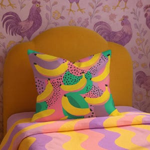 Square pillowcase featuring a bold and playful banana print in a vibrant pop art style. The design includes bright yellow bananas layered over a backdrop of pink, purple, green, and teal with dotted and speckled textures for a dynamic, retro-inspired look. Made of smooth fabric with crisp edges and a snug fit, the pillowcase showcases a saturated, high-contrast palette perfect for maximalist or dopamine decor. Pillow cover only; insert not included.