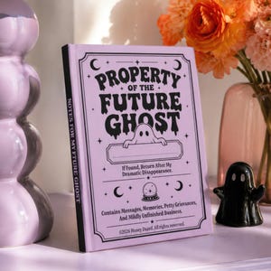 A 5 by 7 inch hardcover journal with a matte pastel purple cover and black printed graphics. The front features a retro inspired illustration of a white ghost character. One design shows the ghost holding a locked book flanked by a lit candle and a skeleton key with text reading Notes For My Future Ghost. The other shows the ghost peeking over a blank label with text reading Property Of The Future Ghost. Both include crescent moons, four point stars, and vintage decorative border frames.