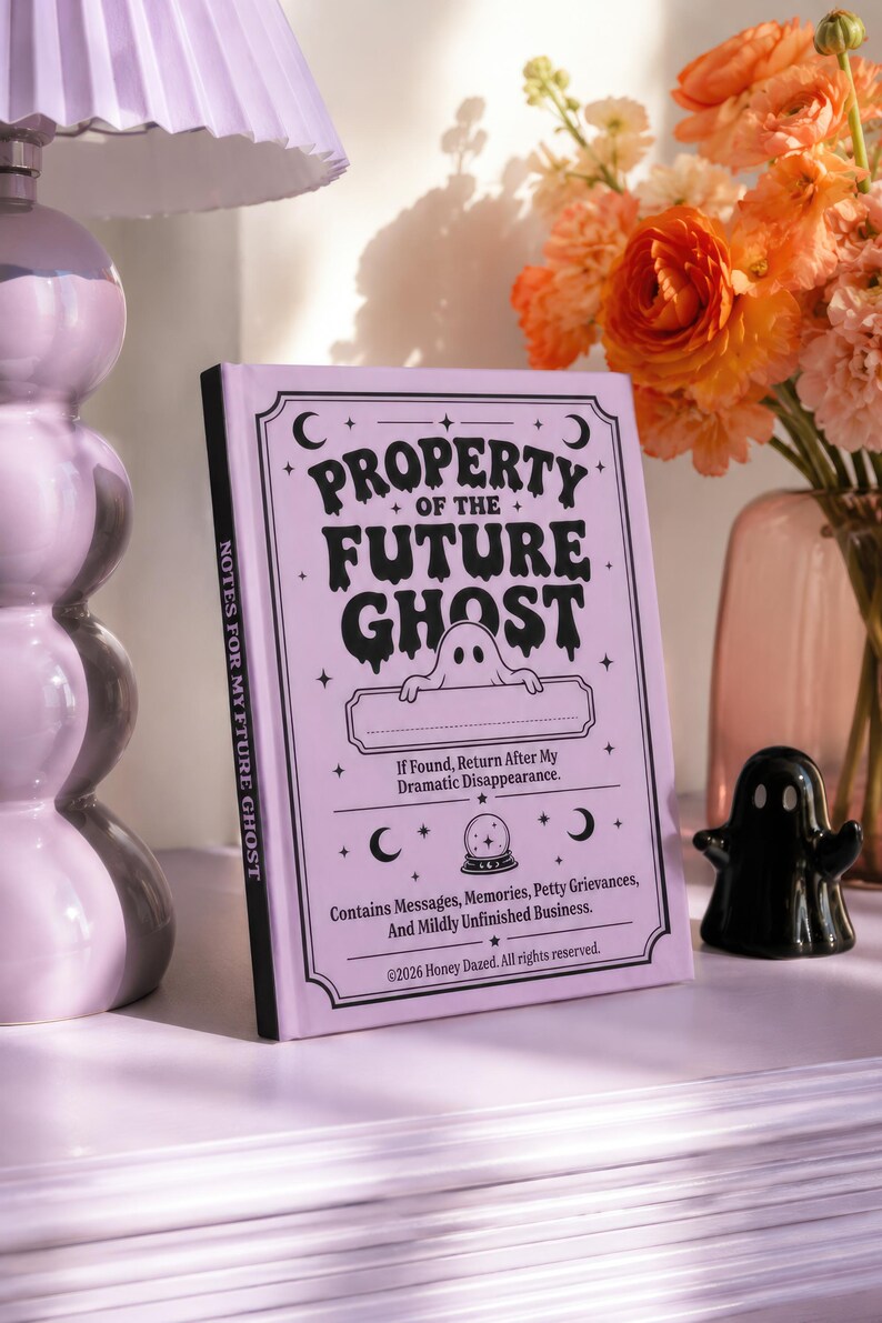 A 5 by 7 inch hardcover journal with a matte pastel purple cover and black printed graphics. The front features a retro inspired illustration of a white ghost character. One design shows the ghost holding a locked book flanked by a lit candle and a skeleton key with text reading Notes For My Future Ghost. The other shows the ghost peeking over a blank label with text reading Property Of The Future Ghost. Both include crescent moons, four point stars, and vintage decorative border frames.