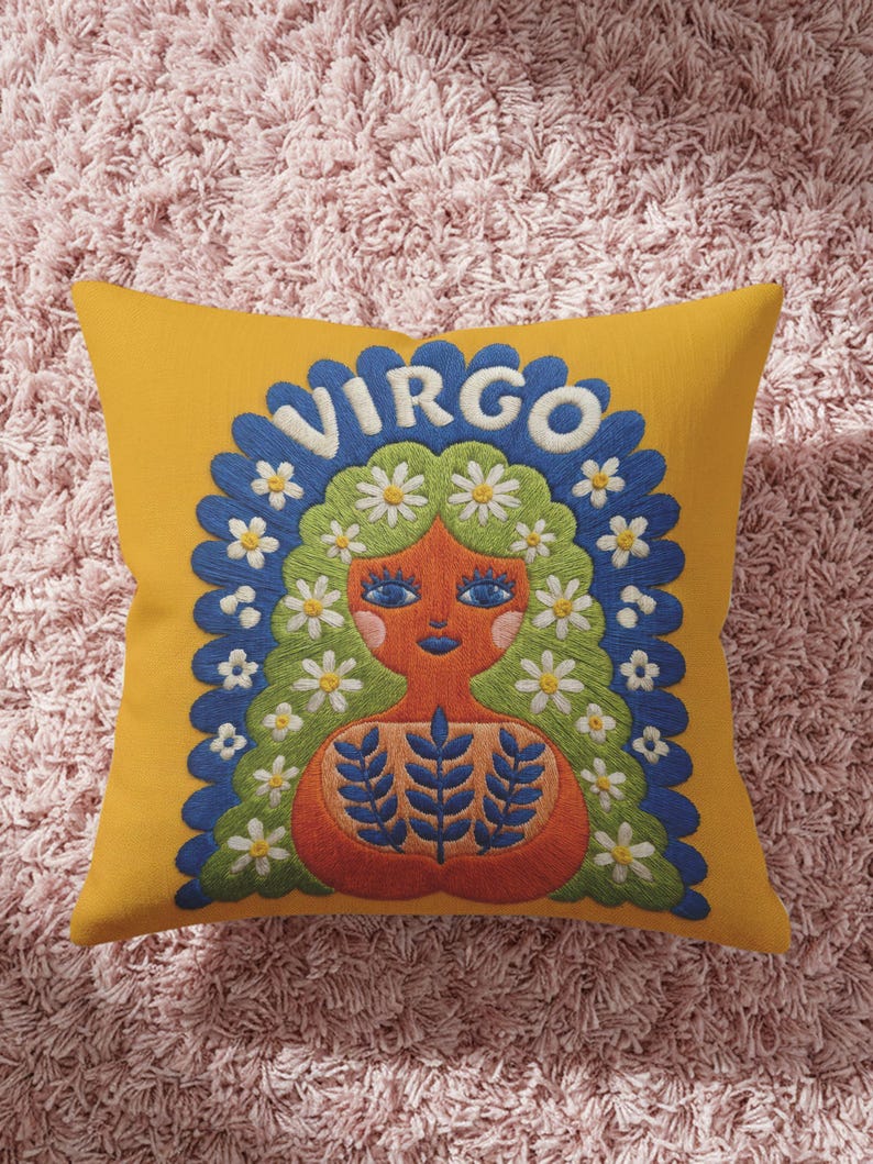 A square throw pillow featuring a vibrant Virgo zodiac design on a golden mustard yellow background. The central illustration shows a terracotta-skinned figure with green hair adorned with white daisies. Blue leaf motifs are printed on the figure’s chest. The word "VIRGO" appears in white bubble letters at the top. The entire design is framed by a royal blue scalloped border, featuring a high-fidelity trompe-l'œil print that mimics 3D embroidery.