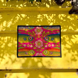 Rectangular indoor outdoor doormat featuring a vibrant hot pink background with a symmetrical maximalist pattern. The design showcases stylized sardines in yellow, lime green, and cobalt blue swimming horizontally towards a central vertical axis of blooming pale pink flowers and green vines. The imagery mimics the texture of vintage needlepoint embroidery but is a flat print on polyester. The mat is framed by a sleek black trim and features a non-slip rubber backing for safety.