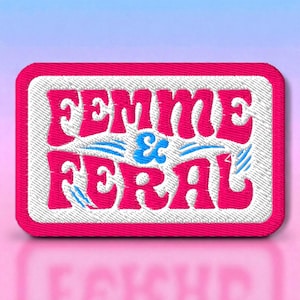 May include: Embroidered patch with the words "FEMME & FERAL" in pink, blue, and white. The patch has a rectangular shape with a pink border and a white stitched background. The text is in a bold, playful font.