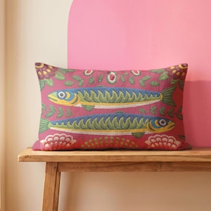 May include: A rectangular throw pillow featuring a vibrant red background with a woven pattern of two blue and yellow fish swimming in opposite directions, surrounded by stylized green leaves and pink floral motifs across the entire surface.