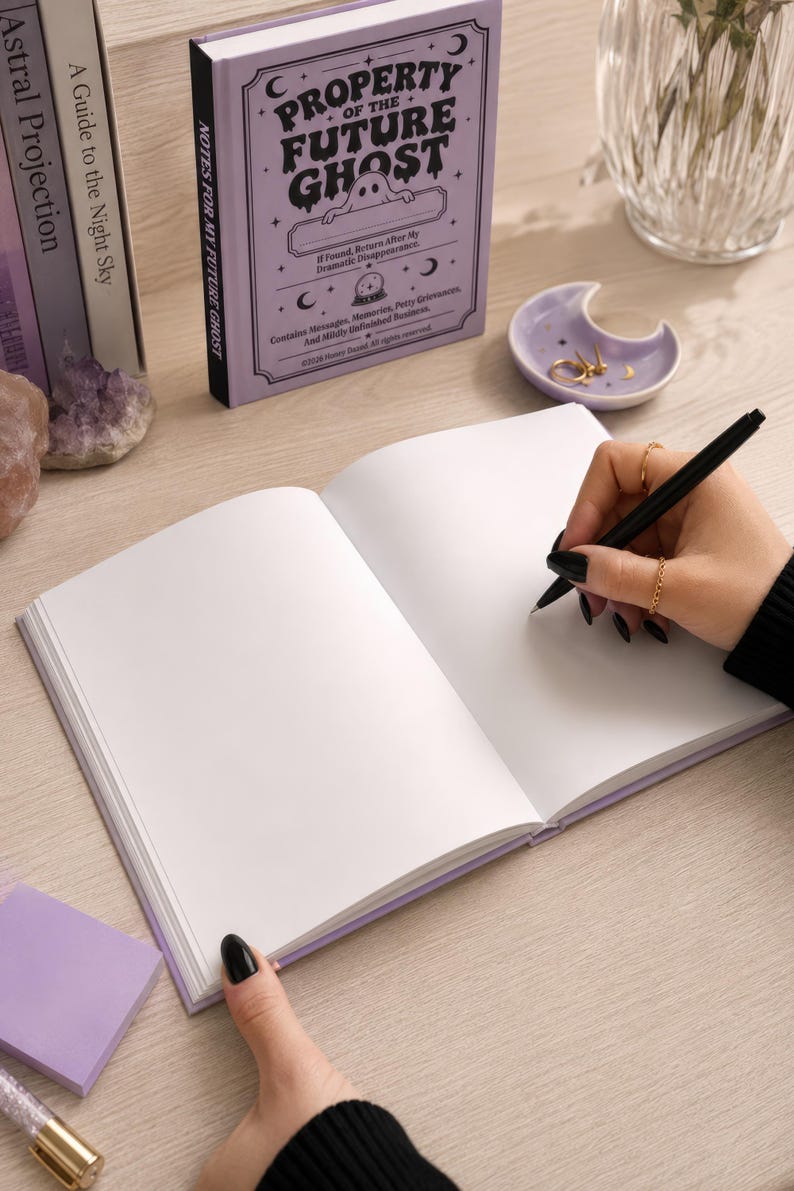 A 5 by 7 inch hardcover journal with a matte pastel purple cover and black printed graphics. The front features a retro inspired illustration of a white ghost character. One design shows the ghost holding a locked book flanked by a lit candle and a skeleton key with text reading Notes For My Future Ghost. The other shows the ghost peeking over a blank label with text reading Property Of The Future Ghost. Both include crescent moons, four point stars, and vintage decorative border frames.