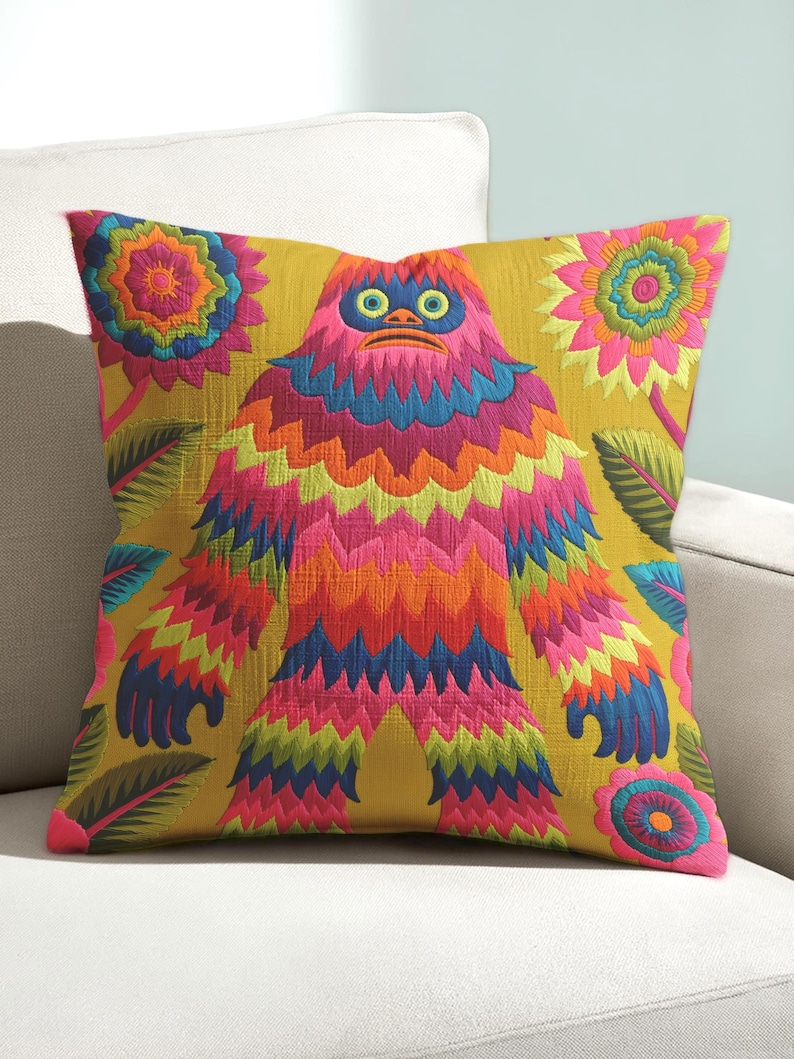 A square faux embroidery pillow featuring a brightly colored maximalist design against a mustard yellow background. In the center stands a stylized, furry Bigfoot or Sasquatch figure rendered in vibrant layers of pink, orange, blue, and lime green with a blue face and yellow eyes. The central creature is surrounded by large, detailed symmetrical pink and blue flowers and leaves. The flat printed fabric creates a highly realistic optical illusion of dimensional crewel embroidery stitches.