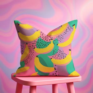 Square pillowcase featuring a bold and playful banana print in a vibrant pop art style. The design includes bright yellow bananas layered over a backdrop of pink, purple, green, and teal with dotted and speckled textures for a dynamic, retro-inspired look. Made of smooth fabric with crisp edges and a snug fit, the pillowcase showcases a saturated, high-contrast palette perfect for maximalist or dopamine decor. Pillow cover only; insert not included.