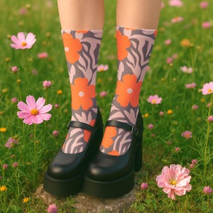 Puede incluir: Zapatos Mary Jane negros con plataforma, con correa y hebilla, combinados con calcetines grises con grandes estampados de flores naranjas. Los zapatos se usan en un campo cubierto de hierba con flores rosas.