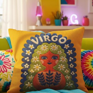 A square throw pillow featuring a vibrant Virgo zodiac design on a golden mustard yellow background. The central illustration shows a terracotta-skinned figure with green hair adorned with white daisies. Blue leaf motifs are printed on the figure’s chest. The word "VIRGO" appears in white bubble letters at the top. The entire design is framed by a royal blue scalloped border, featuring a high-fidelity trompe-l'œil print that mimics 3D embroidery.