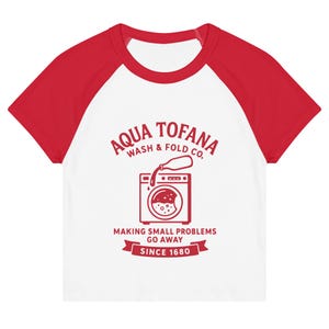 A women's fitted, mid-length micro rib raglan baby tee. The tee's body is solid white, made from a 1x1 micro-rib fabric.  It features short, set-in sleeves and a crewneck collar binding in a bold, contrasting athletic red. Centered on the chest is a vintage-inspired graphic printed in the same red ink. The design is for the "Aqua Tofana Wash & Fold Co." and features an illustration of an old-fashioned washing machine. Text below the machine reads "Making small problems go away" and "Since 1680."