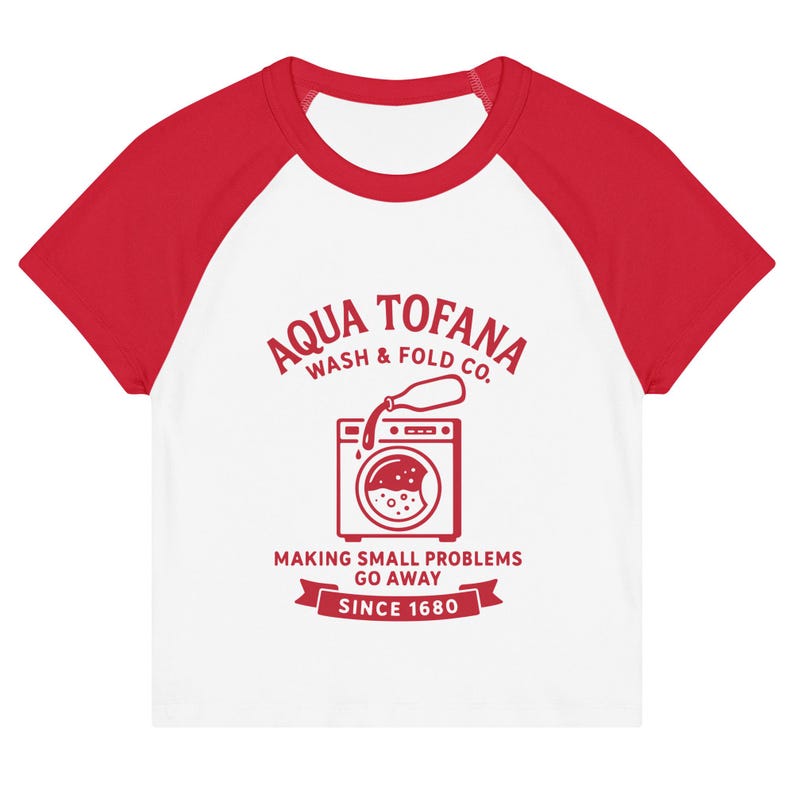 A women's fitted, mid-length micro rib raglan baby tee. The tee's body is solid white, made from a 1x1 micro-rib fabric.  It features short, set-in sleeves and a crewneck collar binding in a bold, contrasting athletic red. Centered on the chest is a vintage-inspired graphic printed in the same red ink. The design is for the "Aqua Tofana Wash & Fold Co." and features an illustration of an old-fashioned washing machine. Text below the machine reads "Making small problems go away" and "Since 1680."