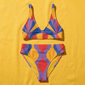 Peut inclure: Un ensemble bikini deux pièces composé d'un haut à encolure dégagée et d'un bas taille haute. Le tissu présente un motif géométrique répétitif dans des tons vifs de rouge, jaune, violet et bleu, avec des rayons de soleil et des courbes.