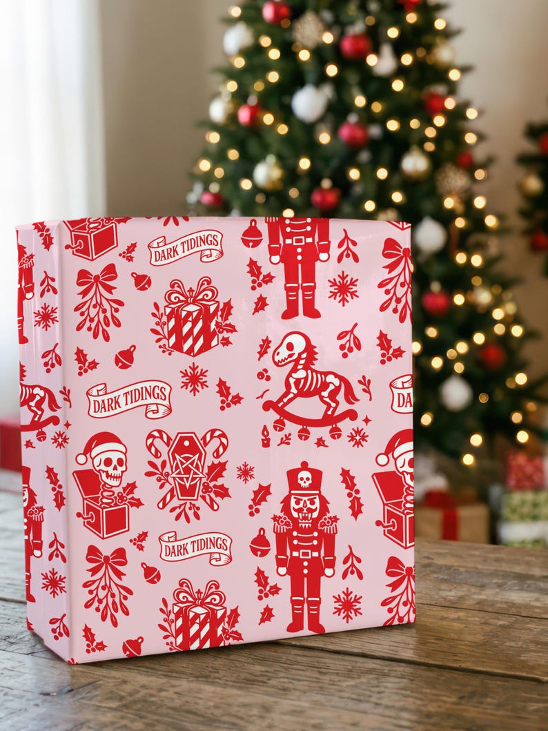 Premium satin finish wrapping paper featuring a repeating pastel goth pattern on a pink background. The design showcases a playful yet spooky aesthetic with high-contrast skeleton nutcrackers, skull jack-in-the-boxes, and rocking horse skeletons in soft pinks, and reds. The paper texture appears semi-glossy. Shown in three available sizes including sheets and rolls, specifically 29 inches wide, suitable for wrapping gifts for holidays, birthdays, or gothic themed occasions.