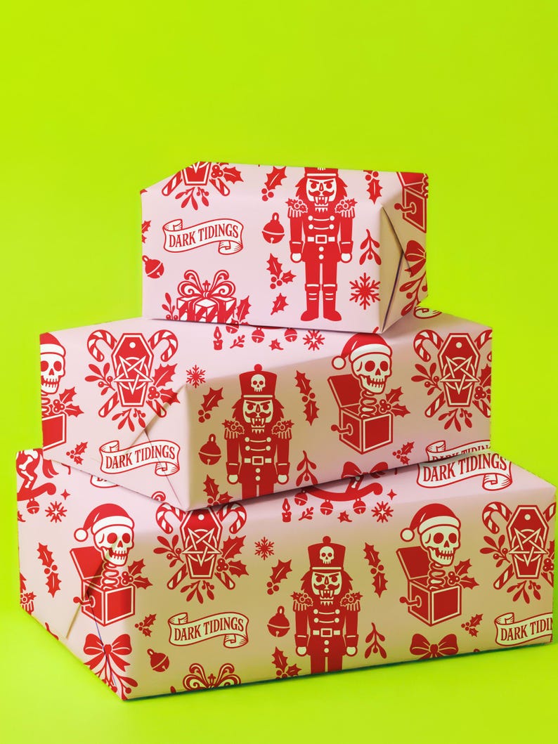 Premium satin finish wrapping paper featuring a repeating pastel goth pattern on a pink background. The design showcases a playful yet spooky aesthetic with high-contrast skeleton nutcrackers, skull jack-in-the-boxes, and rocking horse skeletons in soft pinks, and reds. The paper texture appears semi-glossy. Shown in three available sizes including sheets and rolls, specifically 29 inches wide, suitable for wrapping gifts for holidays, birthdays, or gothic themed occasions.