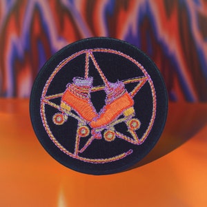 May include: A black embroidered patch with a pentagram design featuring a pair of orange roller skates. The skates are positioned in the center of the pentagram, with the wheels facing outward.