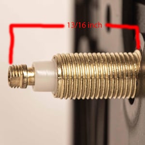 May include: A close-up of a gold-colored metal threaded rod with a white plastic piece. The rod is 13/16 inch long.
