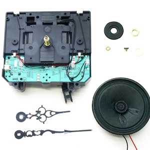 May include: Clock movement kit with black hands, a speaker, and a circuit board. The kit includes a black plastic clock movement with a green circuit board, a black speaker, and two black clock hands. The kit also includes a small black plastic washer, a small gold metal washer, and a small gold metal nut.