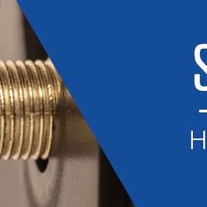 May include: Close-up of a gold-colored solid brass hand shaft. The shaft has a threaded end and a white plastic piece.