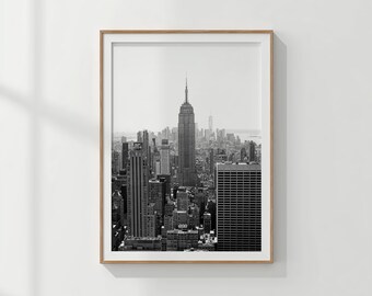 Könnte beinhalten: Schwarz-Weiß-Druck des New Yorker Stadtbildes in einem Rahmen. Das Empire State Building ist der Mittelpunkt, umgeben von anderen Wolkenkratzern. Der Druck befindet sich in einem Holzrahmen.