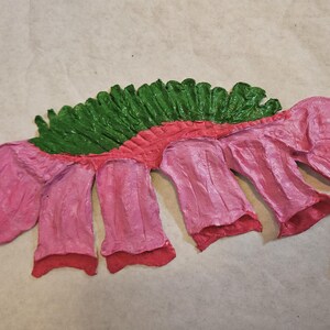 Puede incluir: Una escultura de papel hecha a mano que representa una criatura estilizada. La obra de arte utiliza una paleta de colores vibrantes, con tonos rosas, rojos y verdes. El cuerpo es principalmente rosa, con detalles rojos y una columna vertebral verde texturizada.