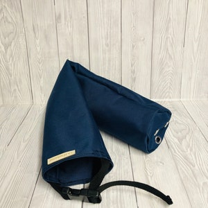 Pu&ograve; includere: Un accessorio in tessuto blu navy di forma cilindrica, dotato di una cinghia nera regolabile con fibbia in plastica, occhielli metallici argentati su un'estremit&agrave; e una piccola etichetta rettangolare beige con il testo J.A.Fashions cucita sul lato.