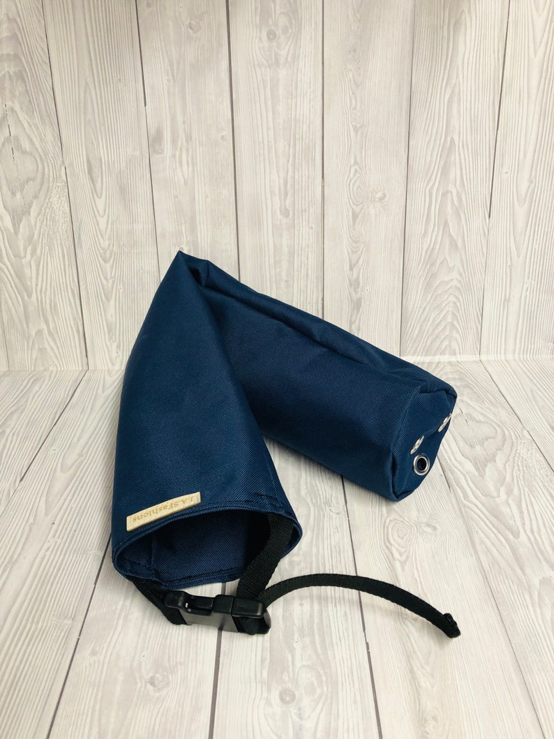 Pu&ograve; includere: Un accessorio in tessuto blu navy di forma cilindrica, dotato di una cinghia nera regolabile con fibbia in plastica, occhielli metallici argentati su un'estremit&agrave; e una piccola etichetta rettangolare beige con il testo J.A.Fashions cucita sul lato.
