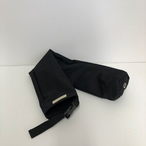 Pu&ograve; includere: Un astuccio cilindrico in tessuto nero dotato di chiusura con fibbia in plastica, cinturino in nylon nero regolabile e una piccola etichetta rettangolare con il testo L.A. FASHIONS. L'estremit&agrave; dell'astuccio presenta un occhiello metallico argentato.