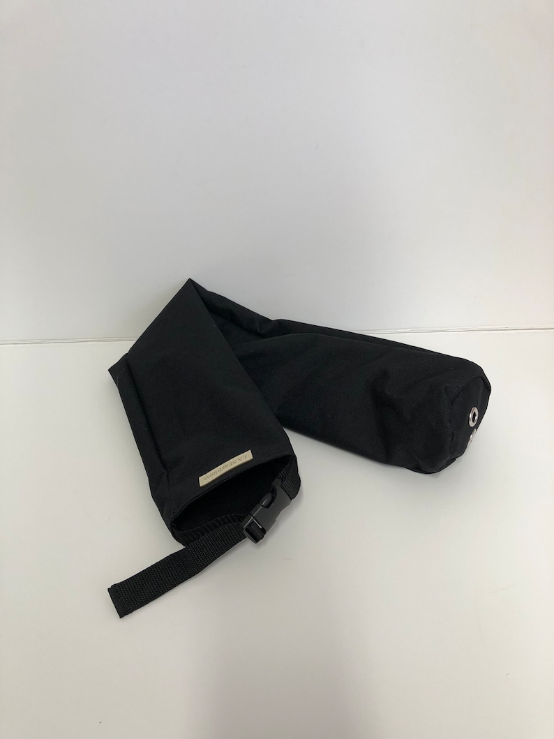 Pu&ograve; includere: Un astuccio cilindrico in tessuto nero dotato di chiusura con fibbia in plastica, cinturino in nylon nero regolabile e una piccola etichetta rettangolare con il testo L.A. FASHIONS. L'estremit&agrave; dell'astuccio presenta un occhiello metallico argentato.