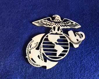 May include: A wooden cutout of the United States Marine Corps emblem, featuring an eagle perched atop a globe with an anchor wrapped around it.