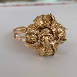 May include: A gold ring with a large, intricate flower design. The flower is made of multiple layers of gold, and the center of the flower has a small, round, gold stone.
