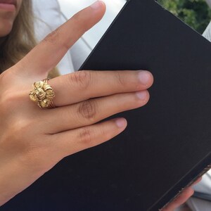 May include: A close-up of a hand wearing a gold ring with a floral design. The hand is holding a black book.