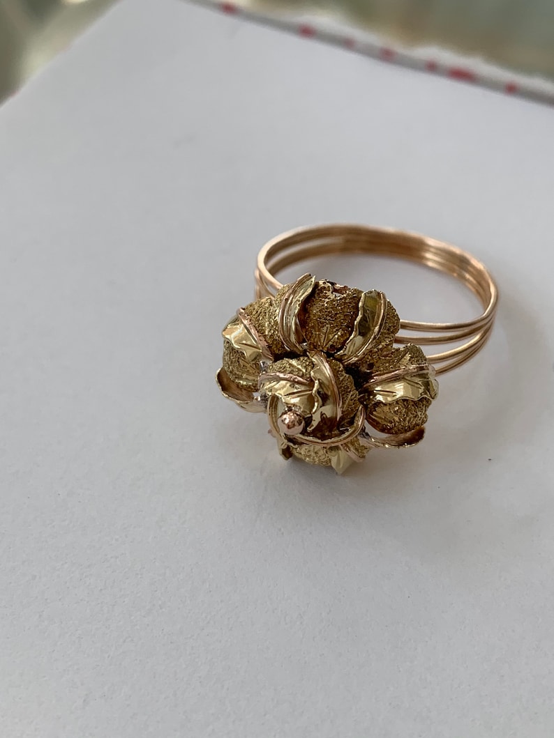 May include: A gold ring with a flower design. The flower is made of multiple leaves that are textured and have a slightly raised surface.