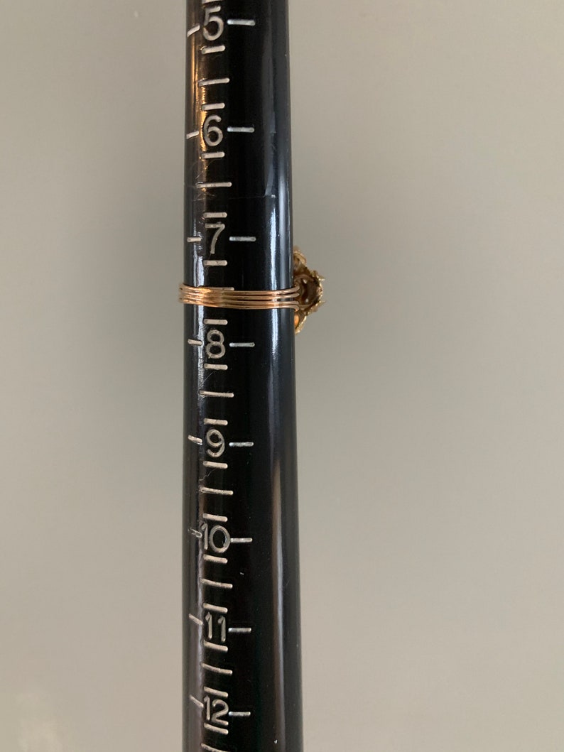 May include: A gold ring with a floral design and a single, clear stone. The ring is shown on a ruler, measuring approximately 8 inches in diameter.