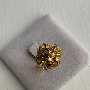 May include: A gold ring with a rose-shaped design. The rose is made of textured gold and has a small diamond in the center.