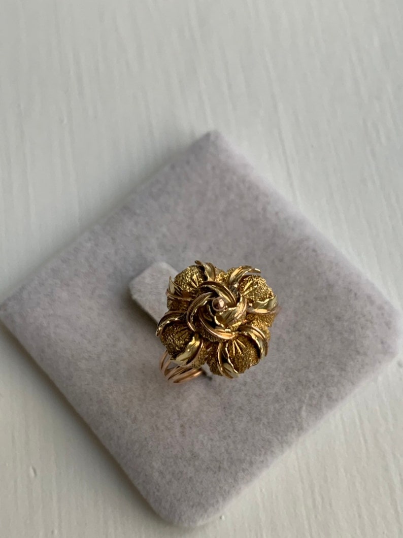May include: A gold ring with a rose-shaped design. The rose is made of textured gold and has a small diamond in the center.