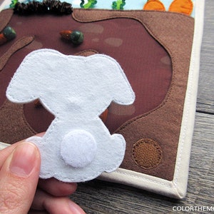 May include: A white felt bunny with a white felt tail, the bunny is attached to a brown felt background with a white felt border.