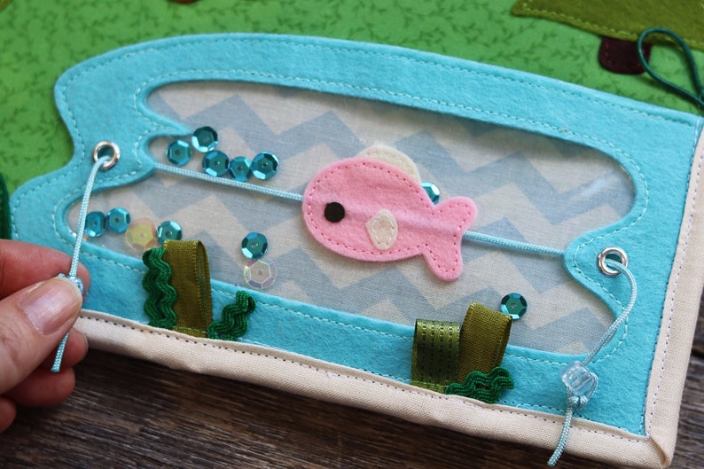 May include: A blue felt board with a pink felt fish, green felt seaweed, and blue sequins. The fish is attached to a string that is threaded through two metal eyelets.
