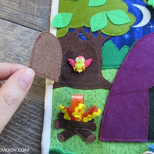 May include: A felt play mat with a purple tent, a brown tree with a birdhouse, a campfire, and green leaves. The tree has a small, pink bird with yellow accents sitting in the birdhouse.